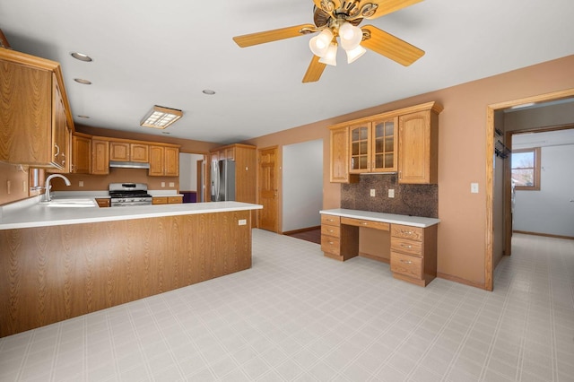 kitchen featuring built in study area, a peninsula, stainless steel appliances, under cabinet range hood, and a sink