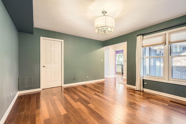 spare room with a notable chandelier and wood-type flooring