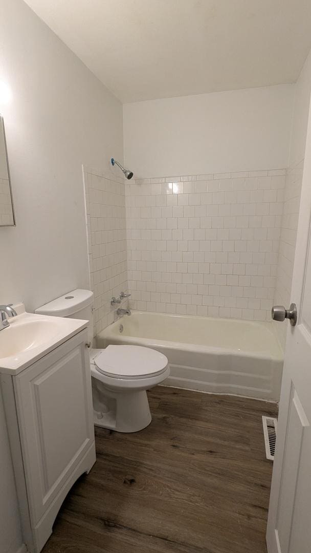 full bathroom with hardwood / wood-style flooring, tiled shower / bath, vanity, and toilet