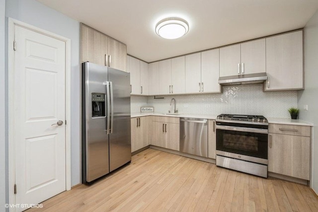 kitchen with light wood-style floors, appliances with stainless steel finishes, light countertops, under cabinet range hood, and a sink