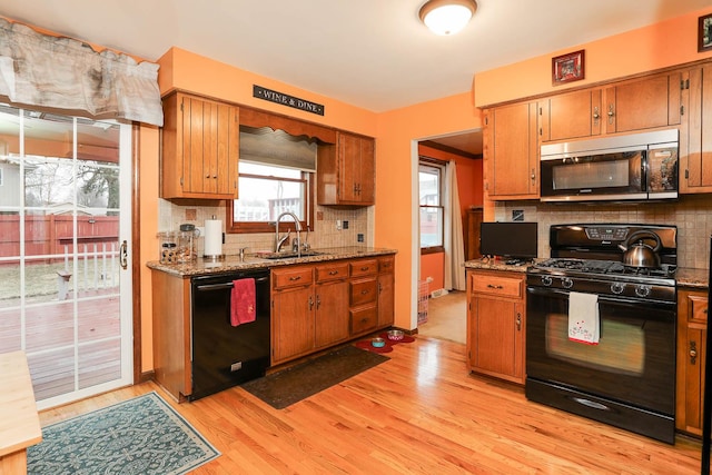 kitchen featuring sink, light wood-type flooring, stone counters, decorative backsplash, and black appliances