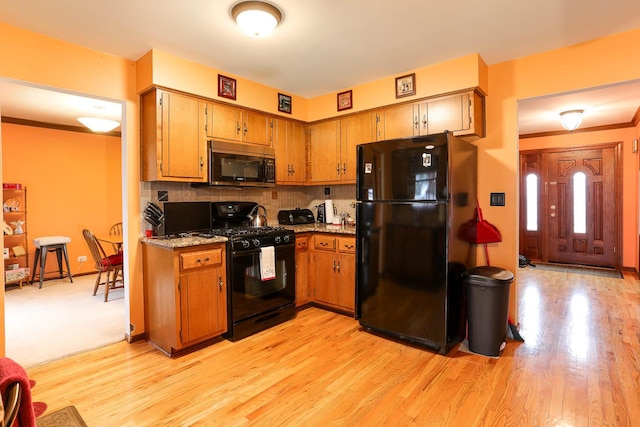 kitchen featuring light stone countertops, backsplash, light wood-type flooring, and black appliances