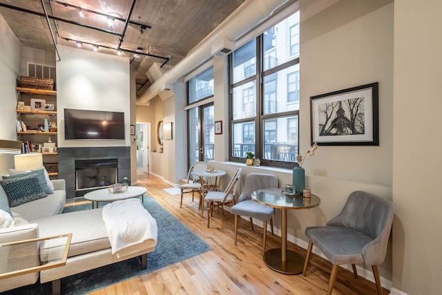 sitting room with a tile fireplace, plenty of natural light, a towering ceiling, and light wood-type flooring