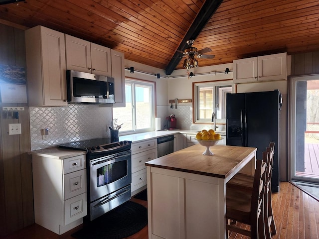 kitchen featuring a breakfast bar, appliances with stainless steel finishes, a center island, white cabinets, and vaulted ceiling