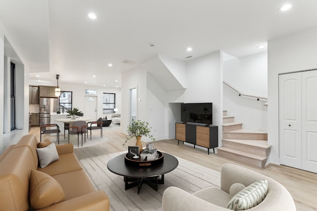 living area with recessed lighting, visible vents, light wood finished floors, and stairs