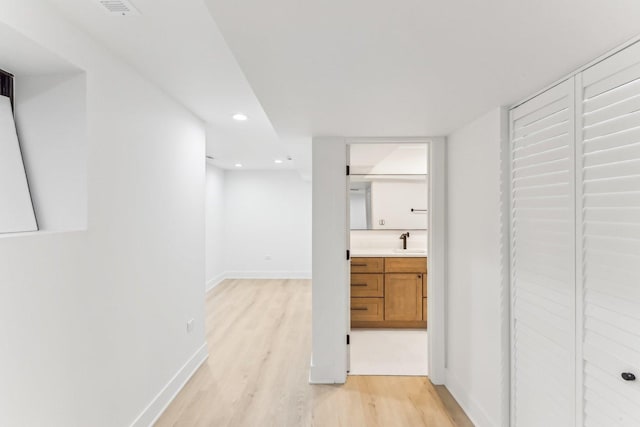 corridor featuring light wood-type flooring, a sink, baseboards, and recessed lighting