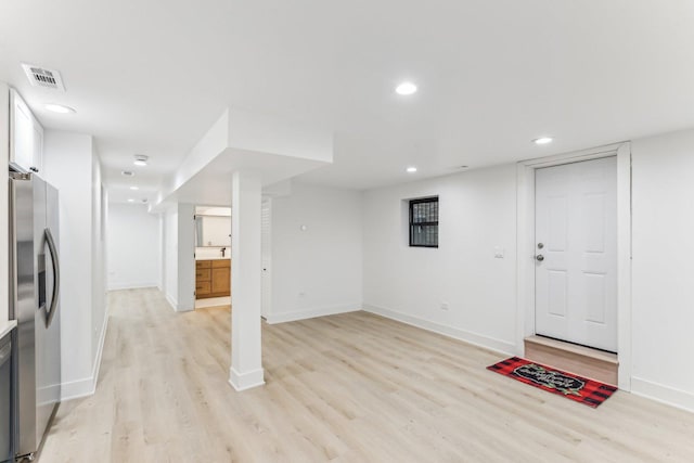 finished below grade area featuring light wood-style floors, stainless steel fridge, visible vents, and recessed lighting