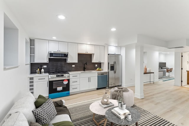 kitchen featuring light wood-type flooring, appliances with stainless steel finishes, white cabinets, and a sink