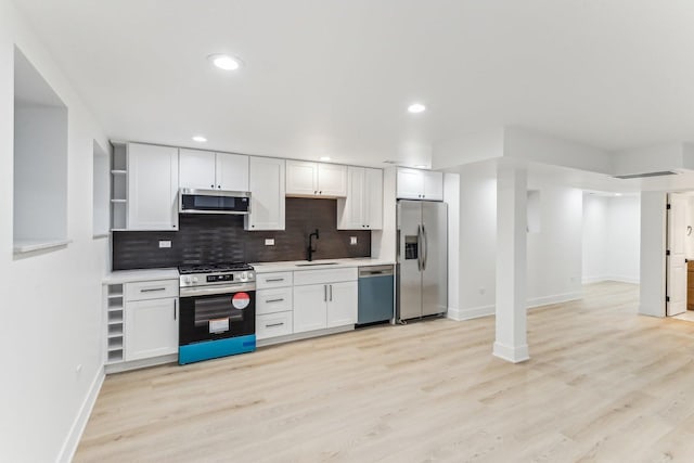 kitchen featuring tasteful backsplash, white cabinets, stainless steel appliances, light wood-style floors, and a sink