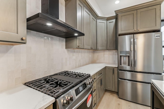 kitchen featuring appliances with stainless steel finishes, decorative backsplash, light wood-style flooring, and wall chimney exhaust hood