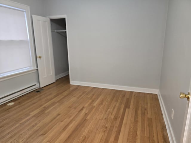 unfurnished bedroom featuring light wood-type flooring, a closet, and a baseboard radiator