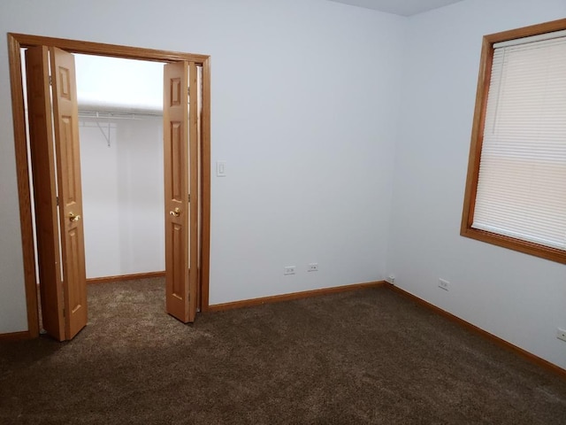 unfurnished bedroom featuring a spacious closet, a closet, and dark colored carpet