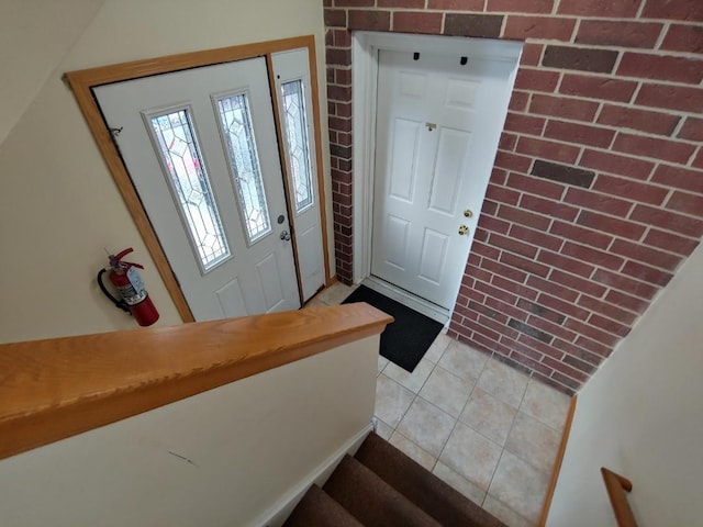 foyer entrance with light tile patterned flooring and brick wall