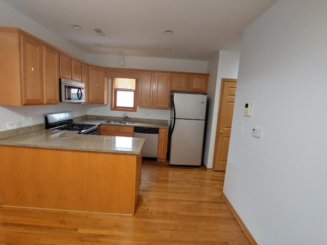 kitchen with appliances with stainless steel finishes, sink, light wood-type flooring, and kitchen peninsula