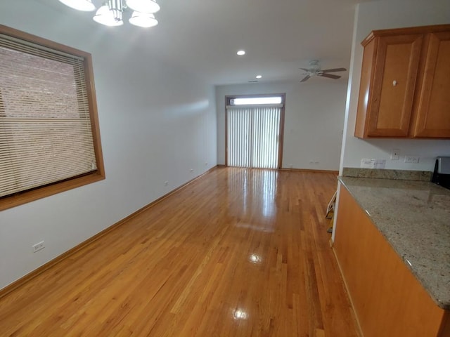 interior space featuring ceiling fan with notable chandelier, light stone counters, and light hardwood / wood-style floors