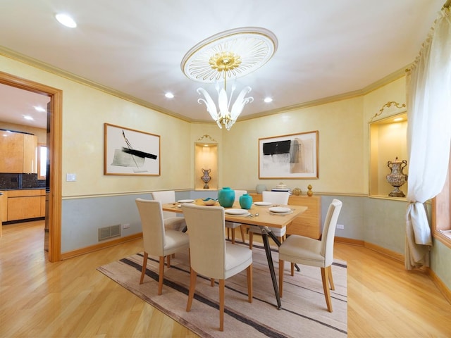 dining area with light wood-style floors, a chandelier, visible vents, and crown molding