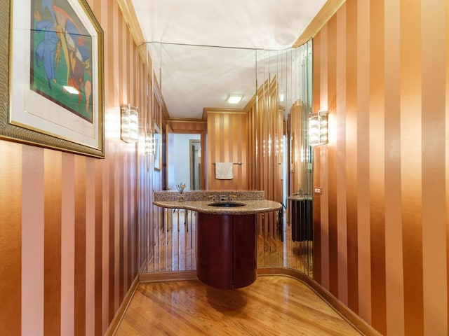 bathroom with wood finished floors, a sink, baseboards, and wallpapered walls