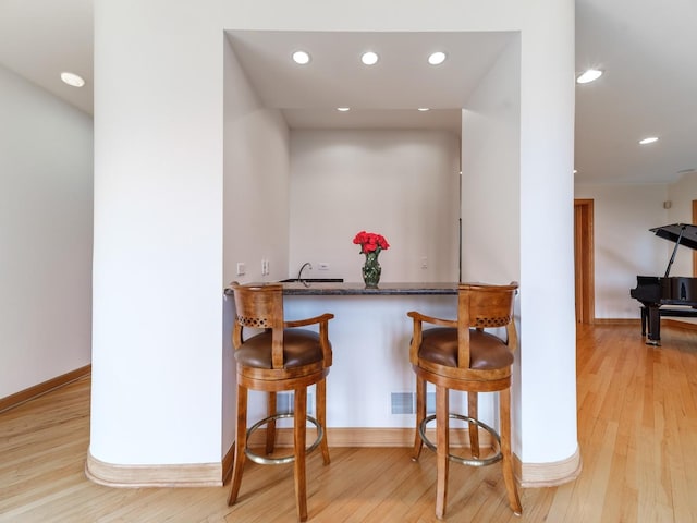 kitchen with baseboards, a breakfast bar area, wood finished floors, and recessed lighting