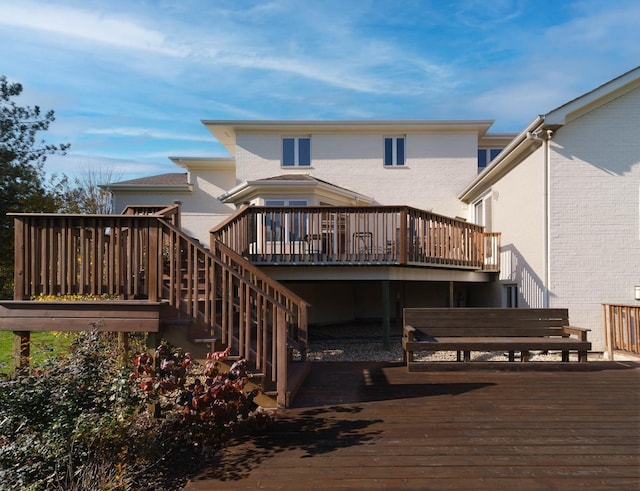 rear view of property featuring a deck, brick siding, and stairway