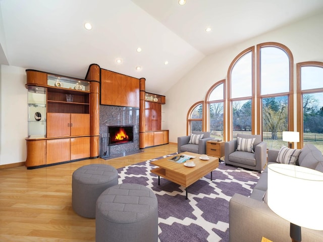 living area featuring high vaulted ceiling, recessed lighting, a high end fireplace, and light wood-style floors