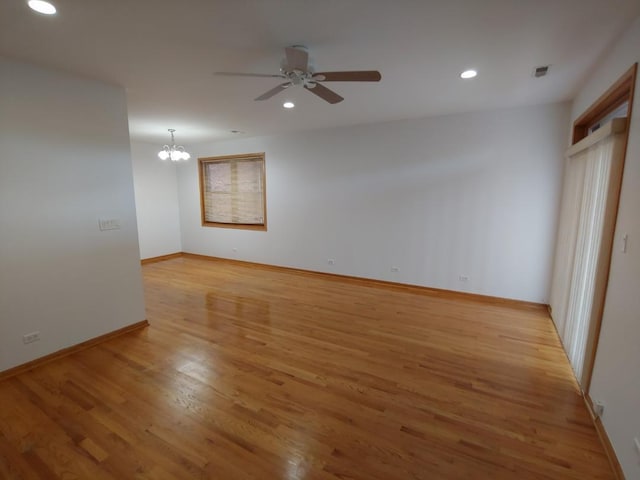 empty room featuring ceiling fan with notable chandelier and light hardwood / wood-style flooring