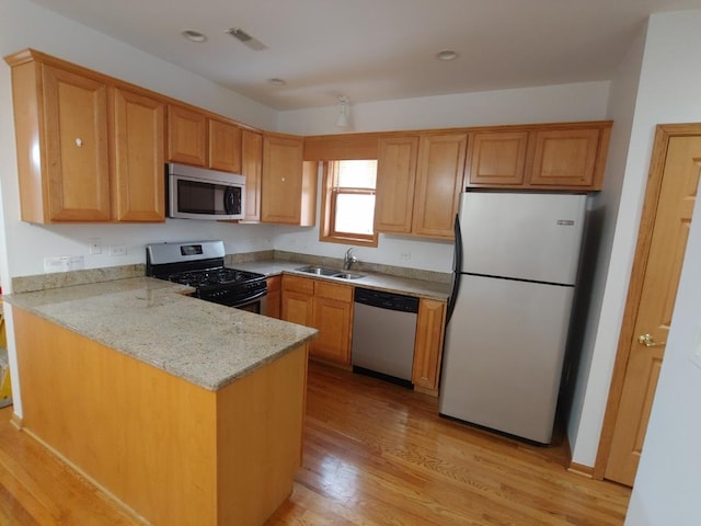 kitchen with sink, light stone counters, kitchen peninsula, stainless steel appliances, and light hardwood / wood-style flooring