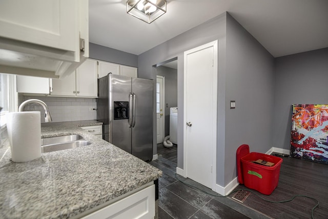 kitchen featuring white cabinetry, baseboards, stainless steel refrigerator with ice dispenser, tasteful backsplash, and washer / dryer