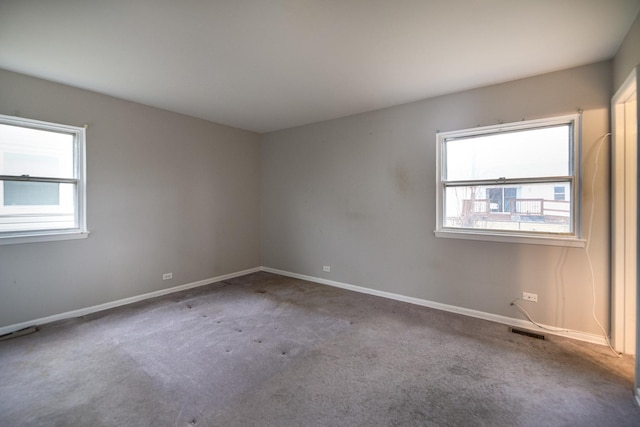 carpeted spare room featuring a wealth of natural light, visible vents, and baseboards