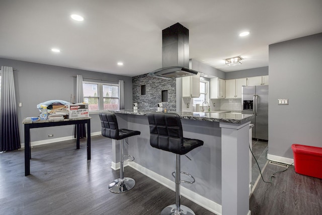 kitchen with tasteful backsplash, stainless steel fridge with ice dispenser, a peninsula, island exhaust hood, and white cabinetry