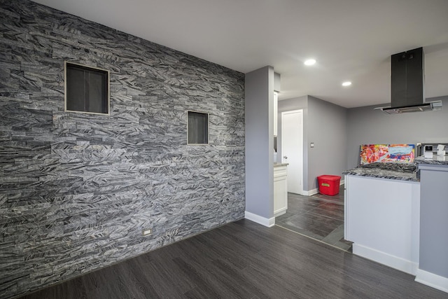 kitchen with baseboards, an accent wall, dark wood-style flooring, range hood, and stone counters