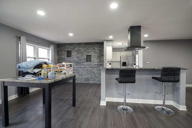 kitchen featuring dark wood finished floors, stainless steel fridge with ice dispenser, island exhaust hood, a kitchen bar, and white cabinetry