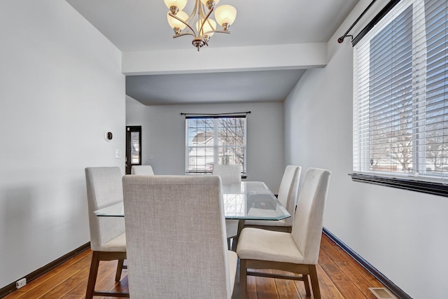 dining space with beam ceiling, hardwood / wood-style flooring, and a chandelier