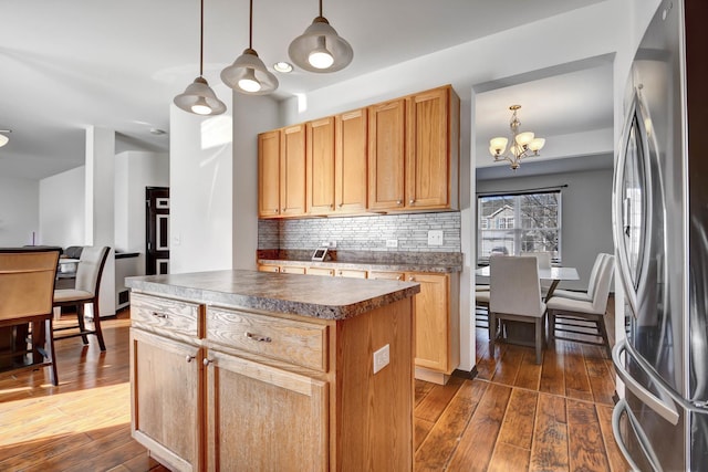 kitchen featuring dark wood-type flooring, tasteful backsplash, a center island, stainless steel refrigerator, and pendant lighting