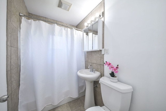 bathroom with a shower with shower curtain, toilet, tile patterned flooring, and tile walls