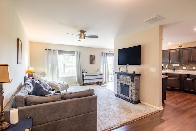 living room featuring ceiling fan, sink, a fireplace, and dark hardwood / wood-style flooring