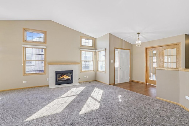 unfurnished living room with high vaulted ceiling, dark colored carpet, and an inviting chandelier