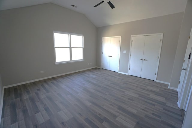 unfurnished bedroom featuring dark wood-type flooring, visible vents, baseboards, vaulted ceiling, and multiple closets