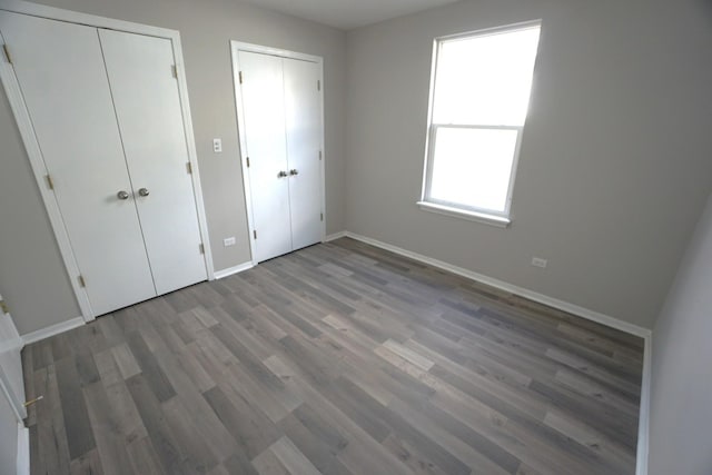 unfurnished bedroom featuring two closets, baseboards, and wood finished floors