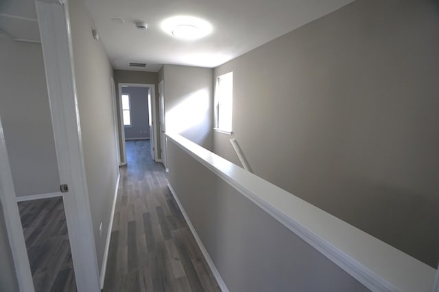 hallway featuring visible vents, baseboards, dark wood-style flooring, and an upstairs landing