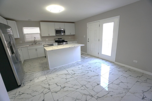 kitchen with stainless steel appliances, a center island, white cabinets, and a sink