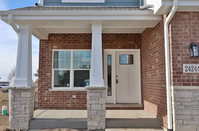 property entrance featuring brick siding, a porch, and a shingled roof