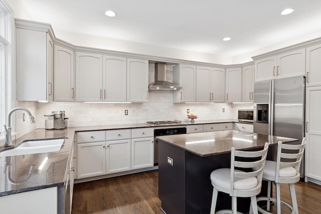 kitchen with sink, a kitchen bar, dark stone counters, a center island, and wall chimney range hood