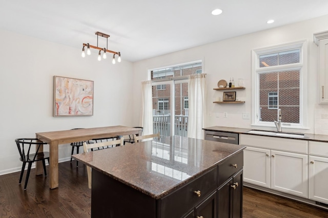 kitchen featuring sink, hanging light fixtures, dark hardwood / wood-style flooring, a kitchen island, and dark stone counters