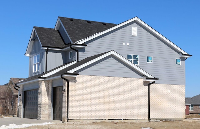 view of home's exterior featuring brick siding, board and batten siding, a garage, and roof with shingles