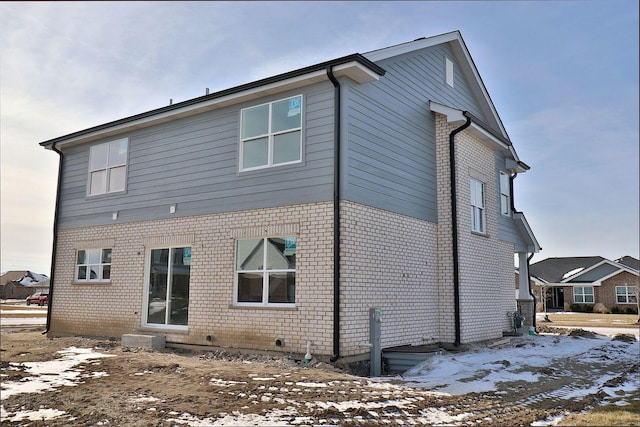 snow covered rear of property featuring brick siding