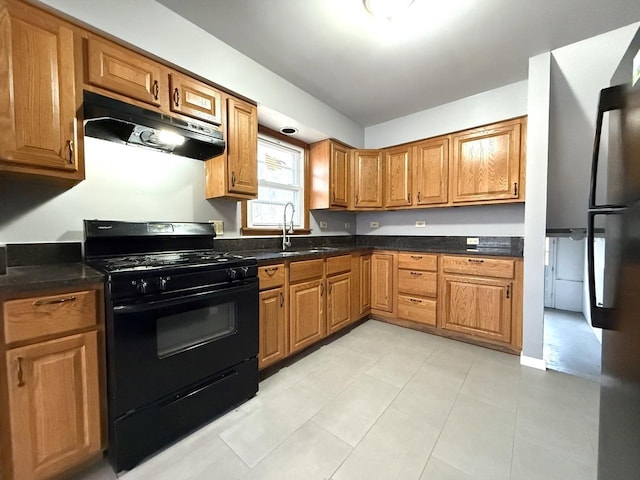 kitchen with sink, dark stone countertops, stainless steel fridge, light tile patterned floors, and gas stove