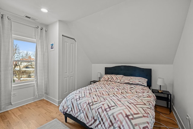 bedroom with hardwood / wood-style floors, lofted ceiling, and a closet