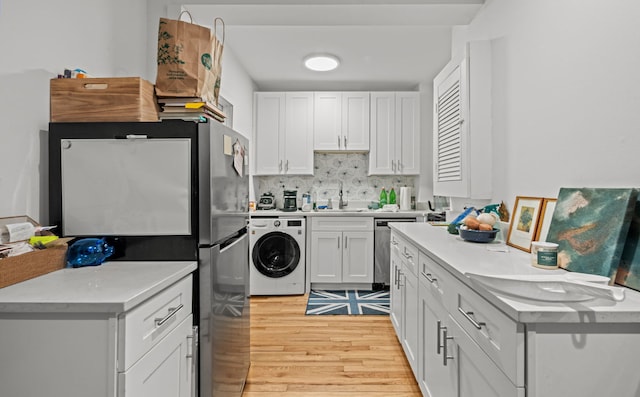 kitchen with stainless steel appliances, washer / dryer, light hardwood / wood-style floors, sink, and white cabinetry