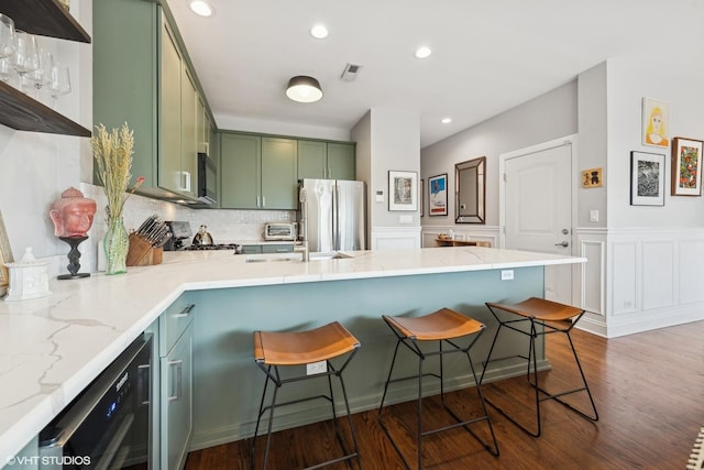 kitchen with dark wood-type flooring, a breakfast bar area, green cabinetry, black appliances, and backsplash