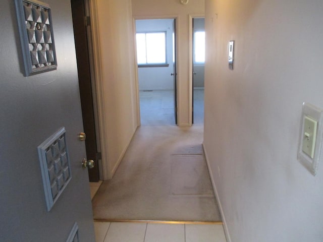 hallway featuring baseboards, light tile patterned floors, and light carpet